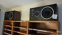 Pair of Fisher speakers on wooden shelving showing right and left speakers with black fronts and wooden sides, each with three drivers including large woofers.