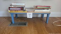 Photo of the 13 books arranged on the small blue shelf showing top and front cover visibility for some titles