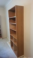 Front-side angle view of the tall MDF bookshelf against a wall showing multiple shelves including bottom divided compartments.