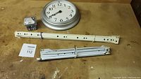 Round wall clock, two metal drawer slides, and box of zinc drill screws on a wooden surface