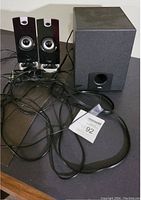 Front view of two black computer speakers with silver around speaker cones and black subwoofer with port, wires included.