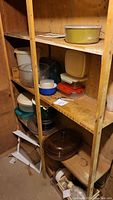 Wooden shelf holding various kitchen containers and bakeware including a large yellow casserole dish on top shelf, multiple plastic containers in the middle and lower shelves, and a brown glass casserole dish on the bottom shelf.