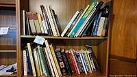 Two wooden bookshelves filled with assorted 56 books on various topics including music, encyclopedias, and brain teasers. Books are in various sizes and colors, mostly hardcover and paperback.