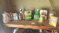 Photo shows a wooden shelf with multiple outdoor cleaning supplies arranged side by side including jugs, spray bottles, and boxes.