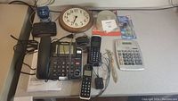 Photo of Panasonic phone set, two cordless handsets, round wall clock, calculator, and various accessories on countertop.