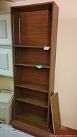 Tall skinny brown MDF bookcase with multiple adjustable shelves, seen from front and side angles.