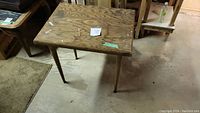 Vintage wooden brown craft table showing tabletop and four legs, placed on basement floor.