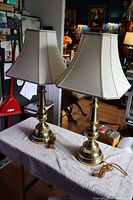 Two brass Stiffel style table lamps with white fabric shades on a towel-covered table in indoor setting.