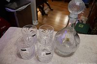 Four Godinger Dublin Collection low ball glasses and one Oberglas Austria glass decanter with stopper displayed on white towel.