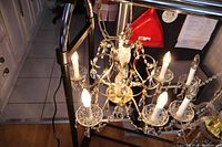 Top perspective of the 5 arm crystal chandelier showing candlestick style bulbs lit, crystal bead strands, and gold-toned frame.