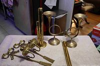 Overview photo showing all six brass items, two wall sconces, two horn-shaped candle holders, and two coin holders arranged on a cloth.
