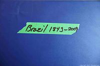 Close-up of green tape label on large blue binder with handwritten text 'Brazil 1843-2009'