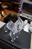 Crystal elephant figurine with raised trunk holding purple crystal ball, angled side view showing facets and clear body