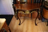 Front angled view of mahogany French style console table showing curved top, painted gold accents on apron and legs, and wood grain finish.