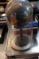 Large glass dome with mounted vintage globe inside, resting on a table. Dome is clear with no visible chips or cracks. Globe shows a cracking flaw.