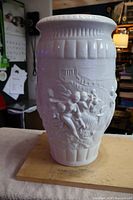 Front side of the large white ceramic vase showing embossed Greek figures and architectural elements in relief.