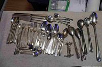 Photo showing various silver plate cutlery including forks, spoons, ladles, and serving utensils laid out on a surface.