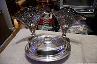 Photo showing two fan-shaped silver-plated vases flanking a covered dish on a table.