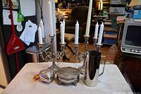 Silver plate lot with candelabras, heart-shaped box, jewelry casket, and water jug displayed on a table with surrounding room background.