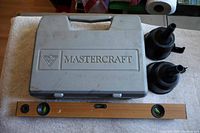 Photo showing gray Mastercraft plastic case with handle, two black plastic funnels, and wooden bubble level arranged on surface