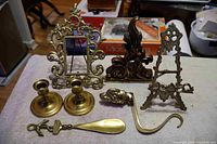 All items arranged on a cloth surface including two candle sticks, an easel, a decorative hand stocking holder, an ornate frame, the shoe horn, and a flame-shaped decorative piece.