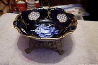 Side view of the vintage blue and white floral dish sitting on the brass stand showing scalloped edges and gold detailing.