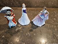 View of all three Royal Dalton porcelain figurines on display showing detailed features and colors.