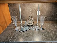 Full view of the candle holders with silver bases and hurricane glass shades, alongside the cruet set on a stone countertop.