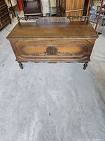 Front view of the antique wooden blanket chest showing carved panel and turned spindle railing.