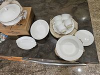 Photo showing the assortment of white bone china dishes, serving bowls, teacups and saucers arranged on a countertop.