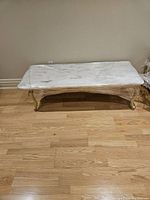Photos showing the full view and close-up of the quartz topped coffee table wrapped in protective plastic, displaying the tabletop and ornate carved wooden legs.