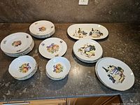 Overview of the full lot including stacks of dinner plates, dessert bowls, and cheese service plates featuring fruit patterns.