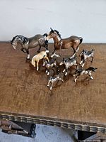 Nine porcelain horse figurines arranged on a wooden table including two large and seven smaller horses in different colors and poses.