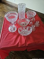 Overview of all 11 crystal pieces on red tablecloth including bowls, vases, bells, and candlesticks