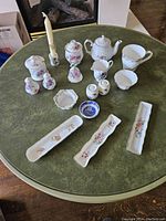 Full view of 17 bone china pieces including teapot, sugar bowl, creamer, shakers, pitchers, trays, bell, and candle holder on a round table.