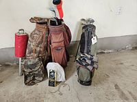 Photo showing all three golf bags standing next to a red golf ball picker and a small package on the floor in front.