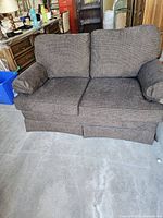 Front view of dark gray love seat showing two seat cushions and two back cushions with rounded armrests and skirted bottom.