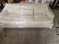 Front view of cream-colored sofa wrapped in plastic film