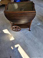 Side view of tea cart showing drop-leaf design, large wooden wheel, small caster wheels, and wooden handles.