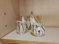 Three-piece Sadler china tea set with teapot, creamer, and sugar bowl featuring gold and black striped pattern with floral accents