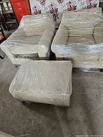 Two chairs and ottoman wrapped in clear plastic on concrete floor