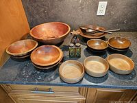 Wide view of entire set showing various wooden salad bowls, wooden salad servers, and decorative wooden containers on a countertop.