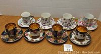 Photo showing eight demitasse cups and saucers arranged in two rows on a table, featuring floral patterns and gold accents.