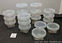 Eighteen small round clear plastic containers stacked in rows, some taller and some shorter, all with clear screw-on threaded lids.