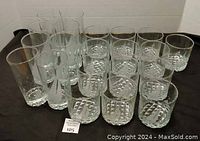 Set of eight tall and thirteen short clear glasses arranged on a black surface showing their shape and design.