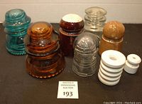 Eight insulators laid out in two rows showing various colors and shapes in glass and ceramic