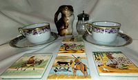 Wide shot of entire lot showing the Bunny creamer, two purple floral cups and saucers, decorative tiles and glass jam pot