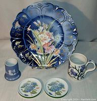 Full shot of the lot showing cobalt blue handled plate with floral design, two Portmeirion butter pat dishes, Scottish thistle mug, and Wedgwood-style jar.