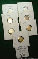 Seven silver small U.S. nickels in white holders with dates marked 1883, 1902, 1907, 1912, 1917, 1919, and 1920 arranged on a green surface.