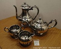 Four piece silver plate tea set including coffee pot, teapot, sugar bowl and creamer, shown on wooden surface.